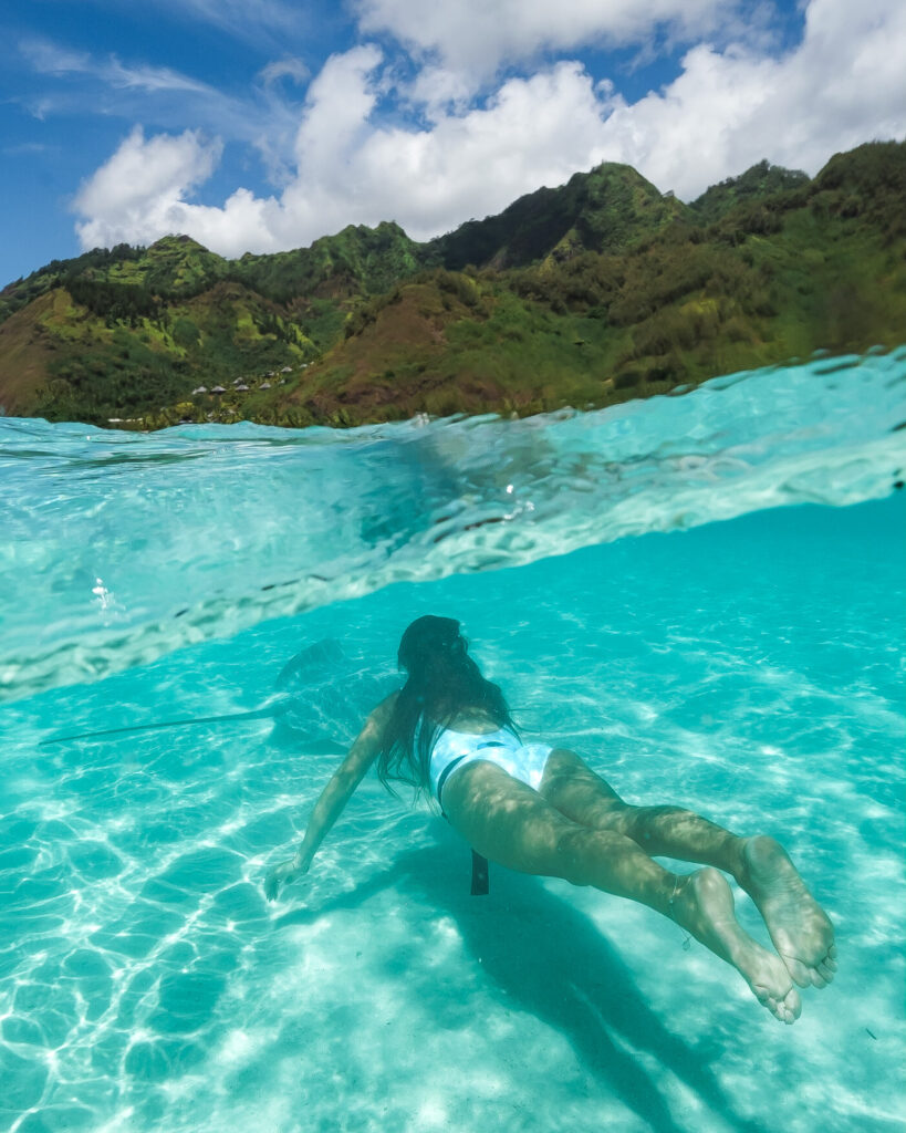 Girl swimming underwater with sting ray in French Polynesia