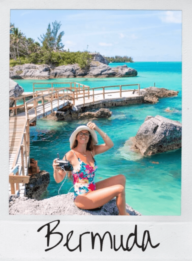 Hi From ashley in Bermuda sitting on a rock with a one piece floral swimsuit and a tan beach babe hat while holding a DJI Mavic 2 pro drone. Vibrant teal and blue waters behind Ashley